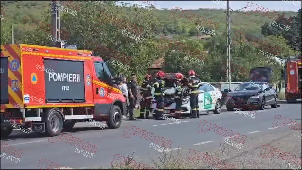 Un camion de pompieri roșu și galben stă pe drum lângă un grup de persoane în uniforme de protecție și două autoturisme.
