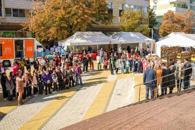 O mulțime de oameni stă în rând pe o stradă pietonală lângă standuri acoperite cu pretrea subterană și un camion portabil.