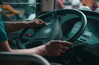Mâinile unui persoană sunt așezate pe volanul unui vehicul de transport public, lângă panoul de bord cu afișaje digitale.