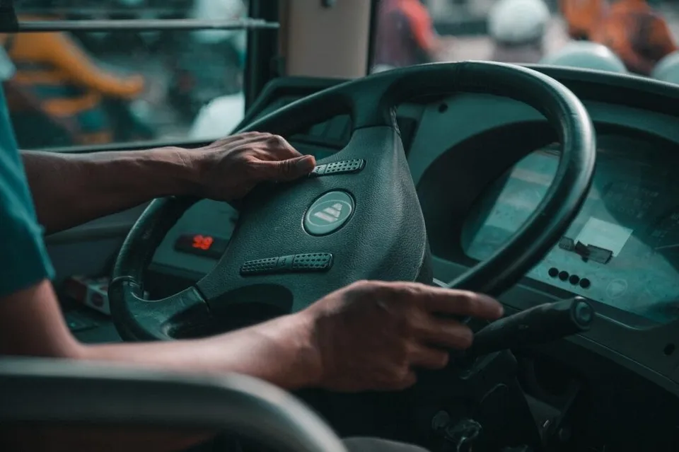 Mâinile unui persoană sunt așezate pe volanul unui vehicul de transport public, lângă panoul de bord cu afișaje digitale.