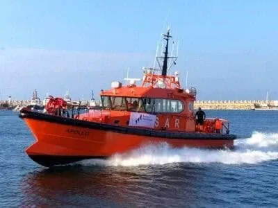 O barcă portocalie cu inscripția SAR navighează pe apă, lăsând în urmă un vârf de spumă albă sub un cer senin.