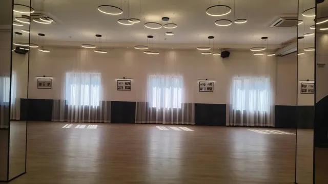 O încăpere spațioasă cu podea de lemn, ferestre acoperite de draperii albe și corpuri de iluminat circulare suspendate de tavanul alb.