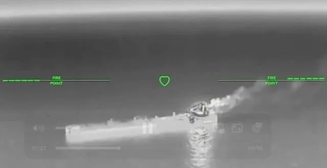 O imagine termică surprinde o navă plutind pe apă, având o zonă luminoasă și fum de la partea din spate, sub un reticul de vizare verde.