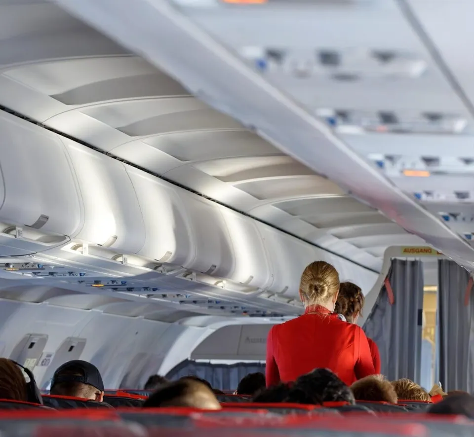 Persoane stau așezate pe scaune în interiorul unei aeronave, sub compartimentele de bagaje de sus.