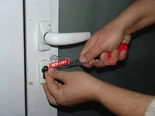Două mâini țin o cheie metalică introdusă într-un cilindru de încuiere de pe o ușă albă.