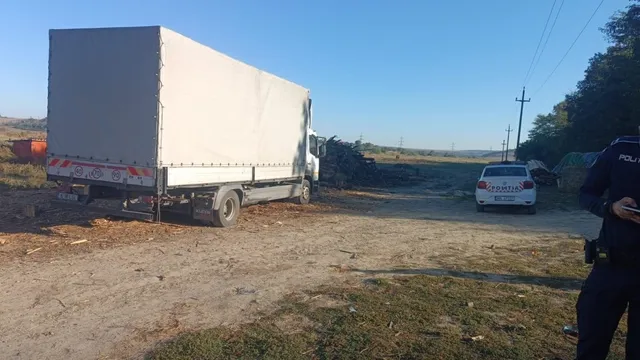 O autoutilitară cu remorcă acoperită cu prelată albă este parcată pe un teren de pământ lângă un autoturism alb sub un cer senin.