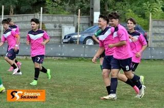 Cinci tineri jucători de fotbal în echipamente roz și negre aleargă pe un teren de iarbă verde.