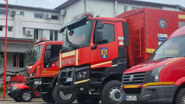 Trei vehicule roșii de intervenție, inclusiv două camioane de pompieri și o dubă, sunt parcate în fața unei clădiri.