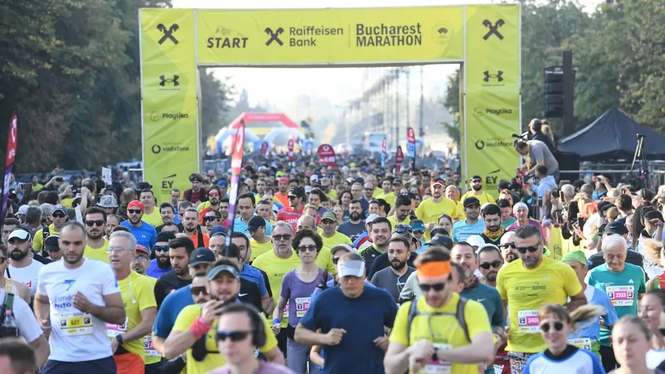 O mulțime de oameni în haine sportive colorate aleargă pe o stradă sub o poartă galbenă marcată cu textul START și Bucharest Marathon.