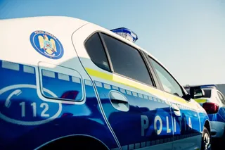 Un autovehicul de poliție albastru și alb este parcat sub un cer senin, fiind vizibilă inscripția POLITIA și numărul 112.