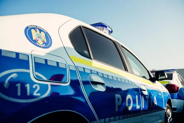 Un autovehicul de poliție albastru și alb este parcat sub un cer senin, fiind vizibilă inscripția POLITIA și numărul 112.