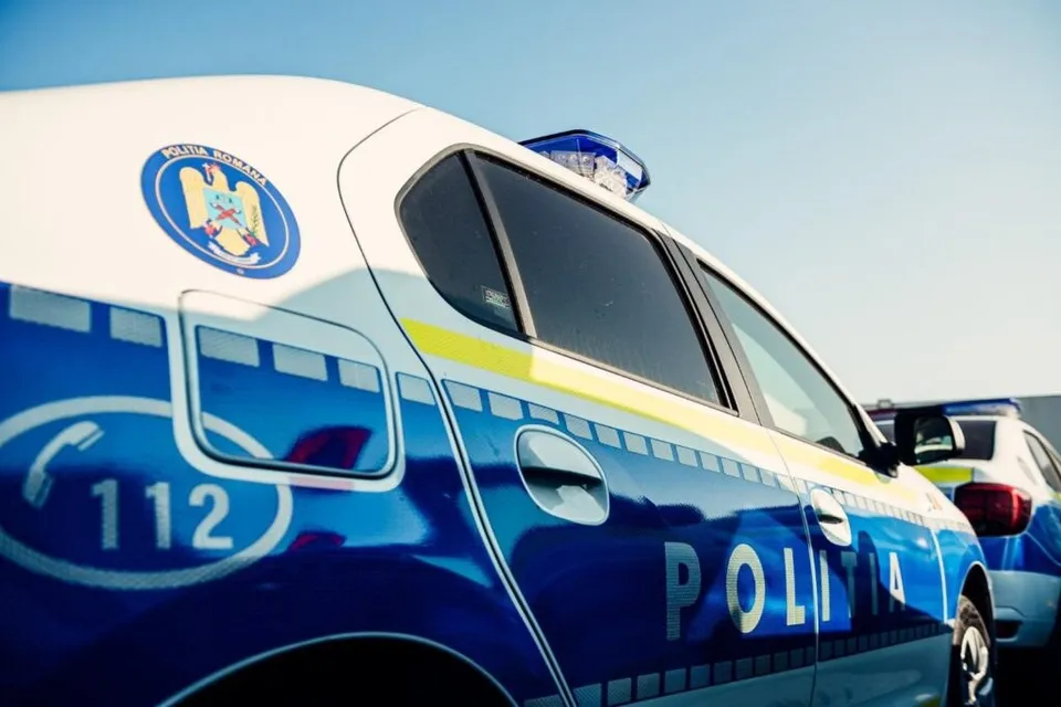 Un autovehicul de poliție albastru și alb este parcat sub un cer senin, fiind vizibilă inscripția POLITIA și numărul 112.