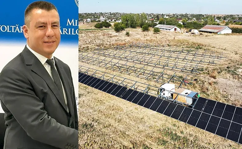 Un bărbat într-un costum gri stă în fața unui fundal albastru, lângă o imagine cu panouri fotovoltaice instalate pe un teren cu iarbă uscată.