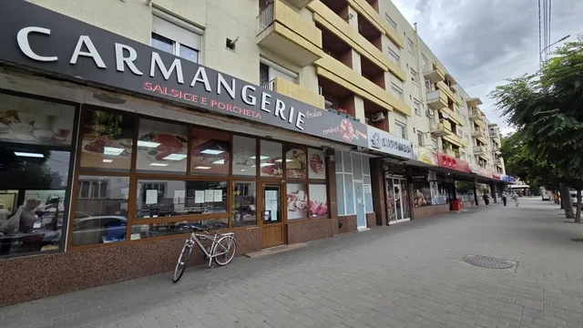 O bicicletă este parcată în fața unei vitrine de magazin de tip carmangerie, aflată la nivelul unei clădiri de apartamente.