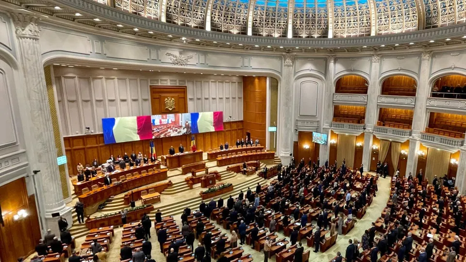 O sală de conferințe circulară cu mulți oameni așezați la mese de lemn sub un plafon înalt și decorat cu elemente arhitecturale clasice.