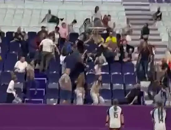 Mai mulți oameni stau în picioare sau se mișcă printre scaunele albastre ale unei tribune într-o sală de sport.