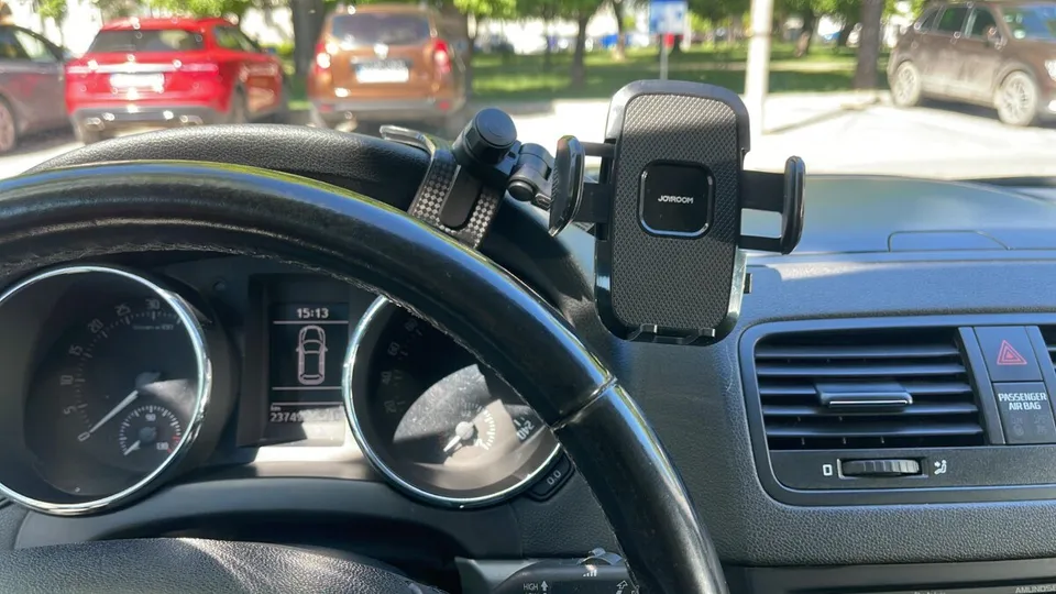 Privire din interiorul unui vehicul asupra volanului, a bordului și a unui suport pentru telefon mobil montat pe panoul de bord.