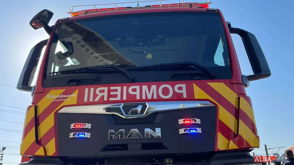 Primul plan al unui camion roșu cu inscripții galbene și albastre, având marca MAN scrisă pe partea frontală.