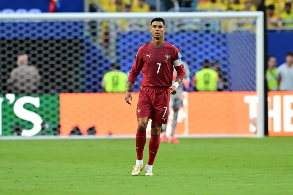 Un fotbalist într-un echipament roșu cu numărul șapte stă pe un teren de fotbal verde în fața unei porți de fotbal.