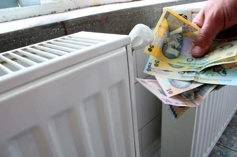 O mână ține mai multe bancnote de lei românești de lângă un calorifer alb.