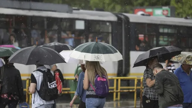 Oamenii merg pe stradă sub umbrele deschise în timp ce un tramvai stă pe șine în fundal.