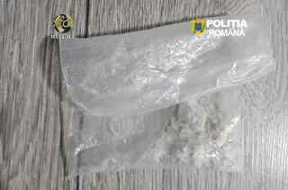 Două pungi mici de plastic transparent conținând o substanță albă granulară sunt așezate pe o suprafață de lemn cu textură gri.