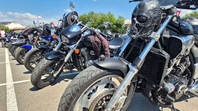 Mai multe motociclete sunt parcate în linie pe un teren asfaltat sub un cer senin.