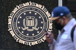 Un sigiliu al Departamentului de Justiție și FBI este montat pe un perete de piatră, în timp ce un bărbat cu șapcă trece în prim-plan.