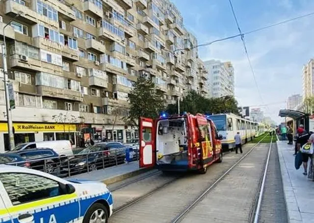 Un vehicul de intervenție roșu cu ușile deschise stă pe șinele de tramvai lângă un tramvai alb și un vehicul de poliție albastru și alb.