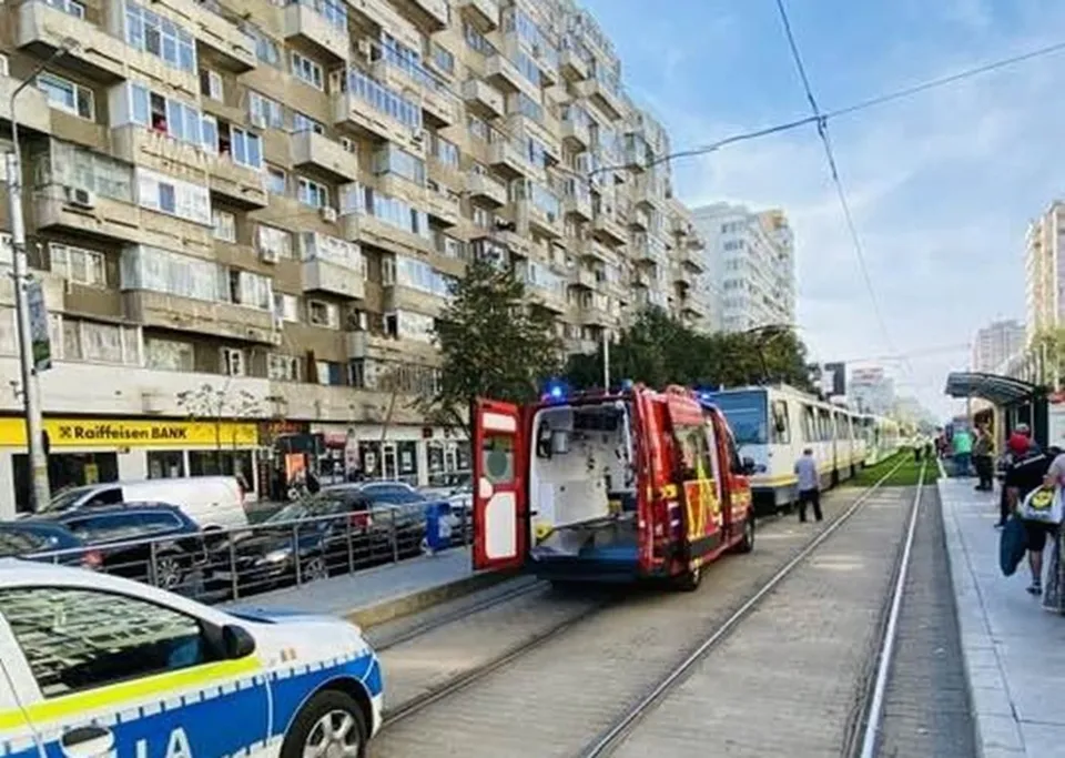 Un vehicul de intervenție roșu cu ușile deschise stă pe șinele de tramvai lângă un tramvai alb și un vehicul de poliție albastru și alb.