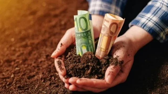 Două mâini țin un pământ întins, în care sunt introduse două bancnote rulate, una verde și una portocalie.