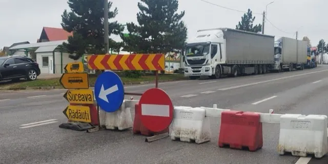 Camioane mari sunt parcate pe marginea unui drum asfaltat lângă bariere de trafic și semne de circulație colorate.