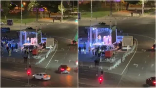 O scenă de noapte prezintă o platformă iluminată cu lumini albastre și albe, aflată pe o stradă cu mașini și semafoare.