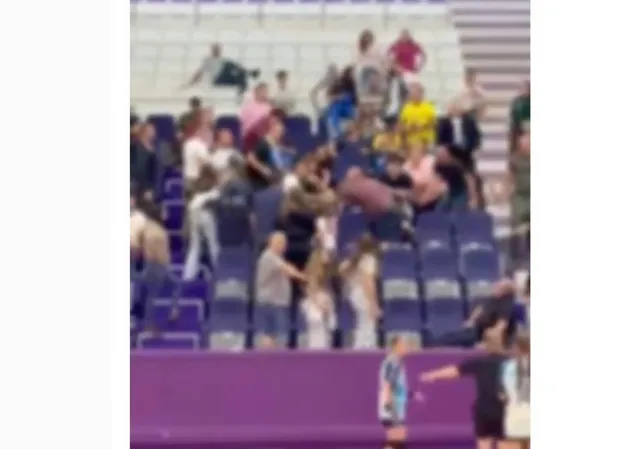 Un grup de persoane este adunat în tribunele unei săli de sport, lângă scaune de culoare albastră.