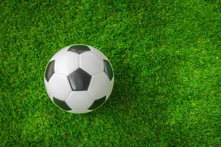 Un fotbal alb cu pete negre este așezat pe un teren de iarbă verde.