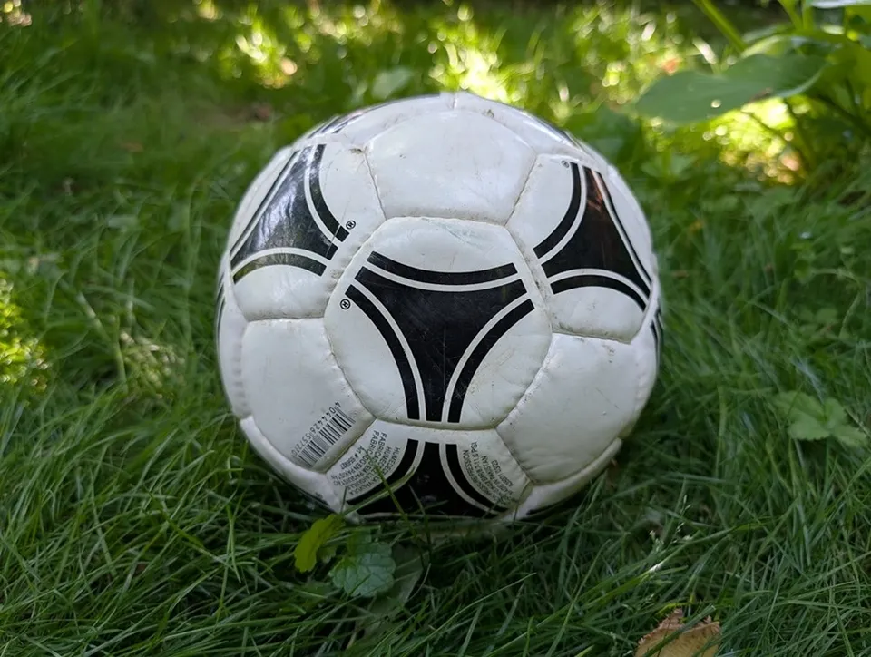 Un fotbal alb cu modele geometrice negre este situat pe iarbă verde.