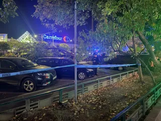 Un copac deformat este așezat peste două mașini și o motocicletă, fiind delimitată zona cu o bandă albastră sub lumini artificiale noaptea.
