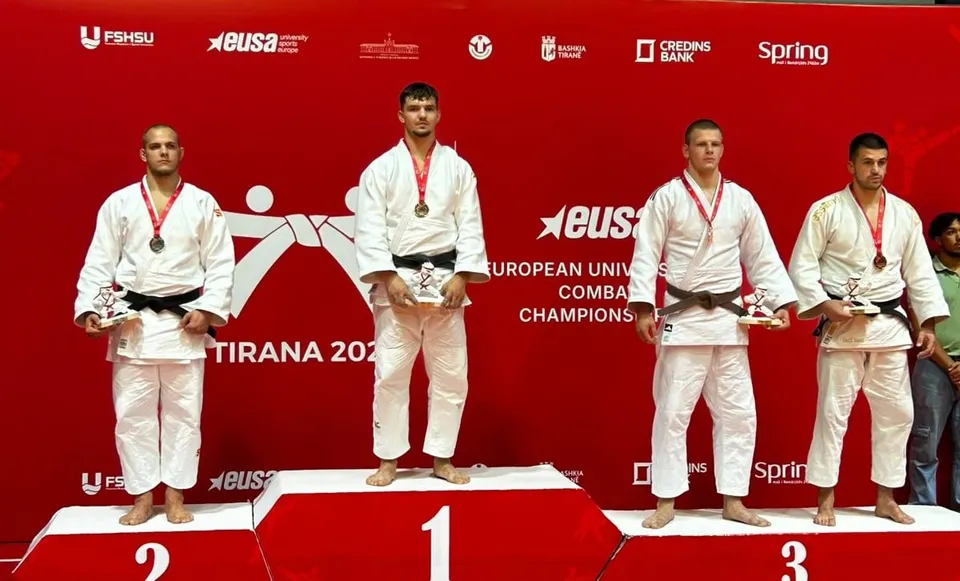 Patru bărbați în costum de judo alb stau pe podiumul de premiere în fața unui fundal roșu.