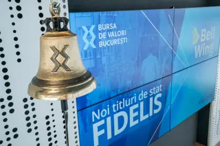 Un clopot metalic cu un simbol gravat este suspendat în fața unor panouri albastre pe care scrie Bursa de Valori București și Fidelis.