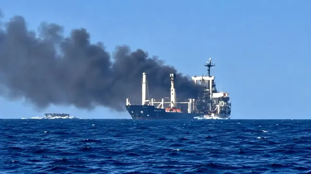 Un vapor mare de culoare închisă emite un nor dens de fum negru pe un ocean sub un cer senin.