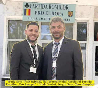 Un bărbat cu părul scurt și costum negru stă lângă un bărbat cu barbă, costum negru și cravată în culorile alb, albastru și gri.