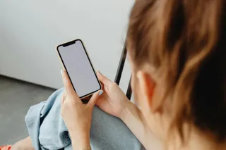 O persoană ține un telefon mobil cu ecranul alb și îl privește de la spate, fiind surprinsă dintr-un unghi lateral.