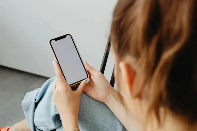 O persoană ține un telefon mobil cu ecranul alb și îl privește de la spate, fiind surprinsă dintr-un unghi lateral.