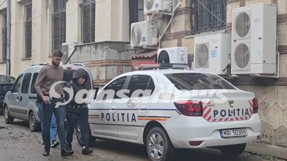 Un bărbat și o femeie merg pe lângă un sedan alb marcat cu inscripția POLITIA și o mașină gri de tip van.