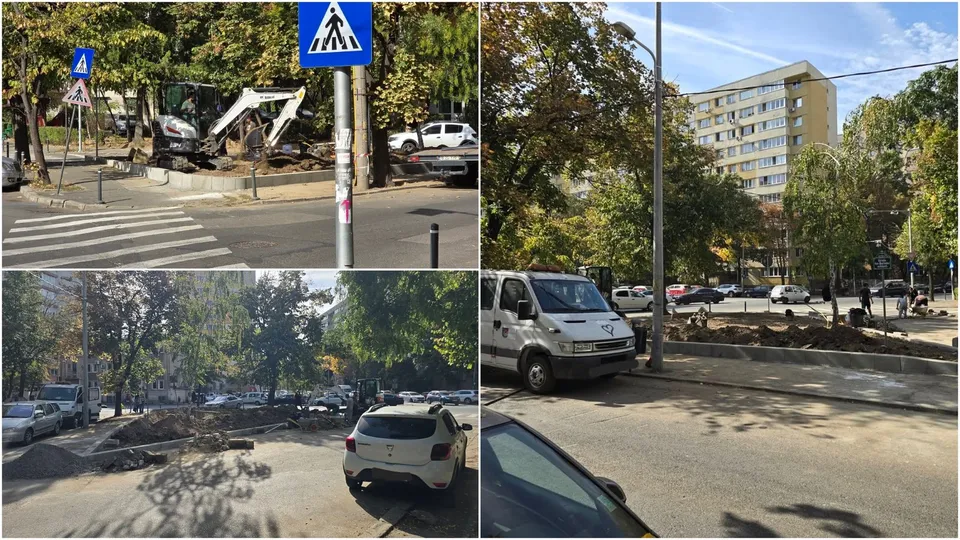 Un excavator alb lucrează pe un trotuar lângă un drum, în timp ce mașini sunt parcate pe o stradă cu copaci și clădiri în fundal.