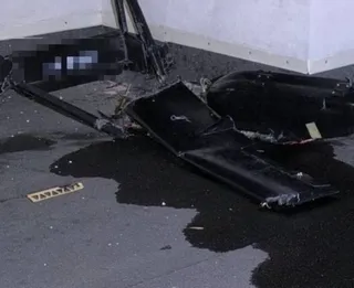 Fragmente negre de un obiect zburător sunt împrăștiate pe o suprafață asfaltată lângă un perete alb.