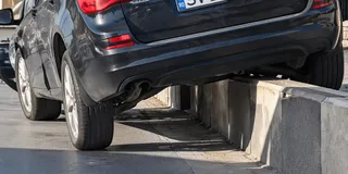 Un autoturism negru este poziționat cu roțile pe asfalt și pe un bord curb, fiind înclinat pe partea dreaptă.