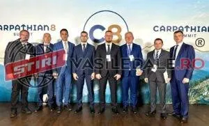 Opt bărbați în costume de culoare închisă stau în rând în fața unui panou publicitar cu text și logo-uri.