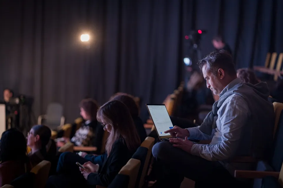 Un bărbat stă așezat într-un auditorium și folosește un dispozitiv digital de tip tabletă.