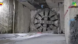 Un utilaj de tunelare circular cu lame metalice este poziționat într-un tunel de beton cu pereți rugoși și podea plată.